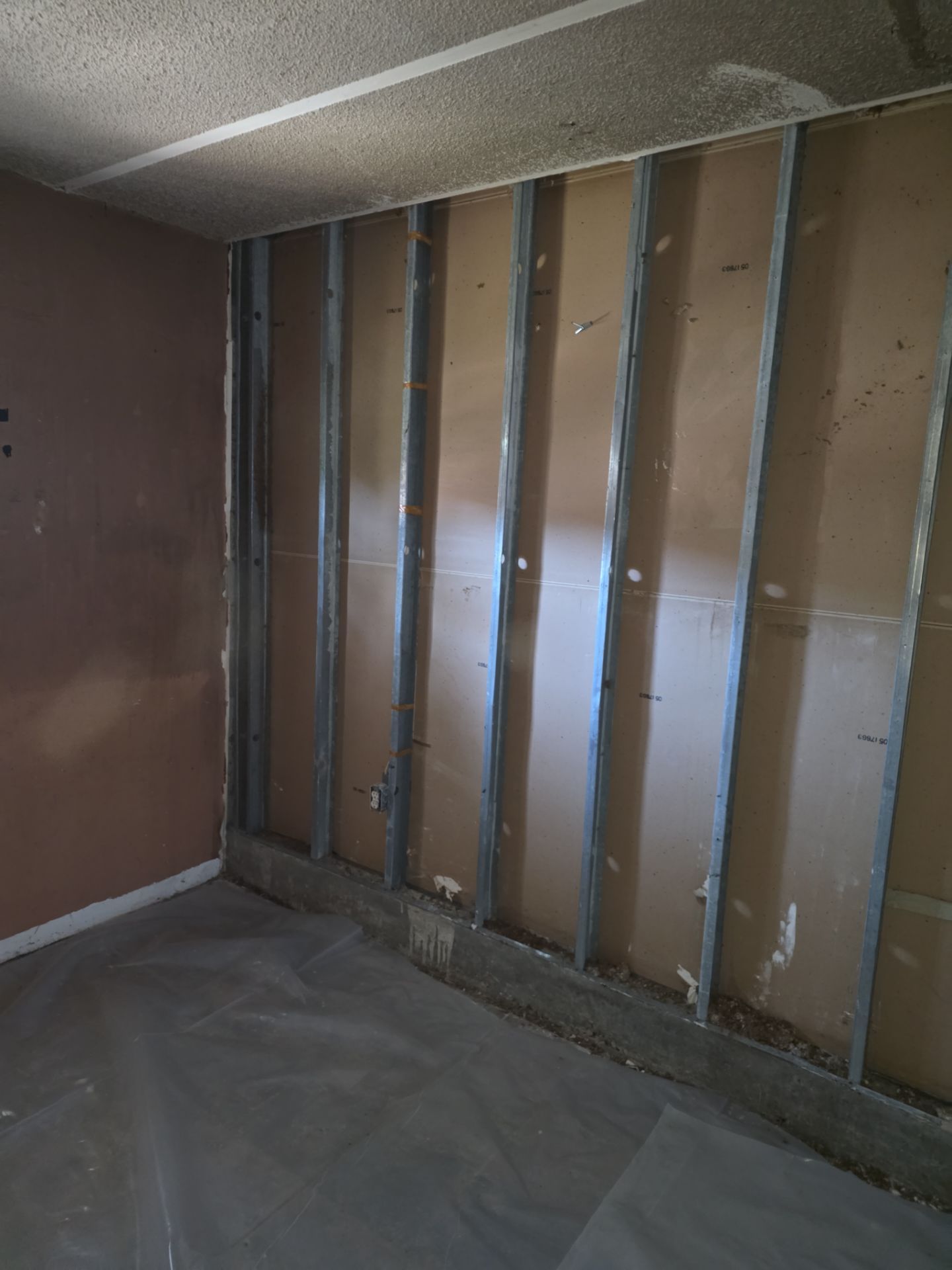 Room stripped to metal studs with plastic sheeting on floor during fire restoration